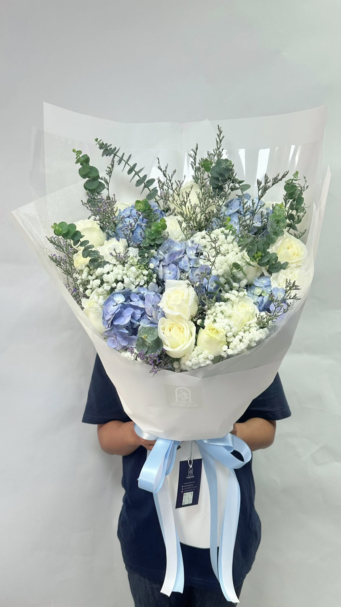 Pale blue hydrangea, white roses, baby's breath and eucalyptus in a white wrap with a soft blue ribbon