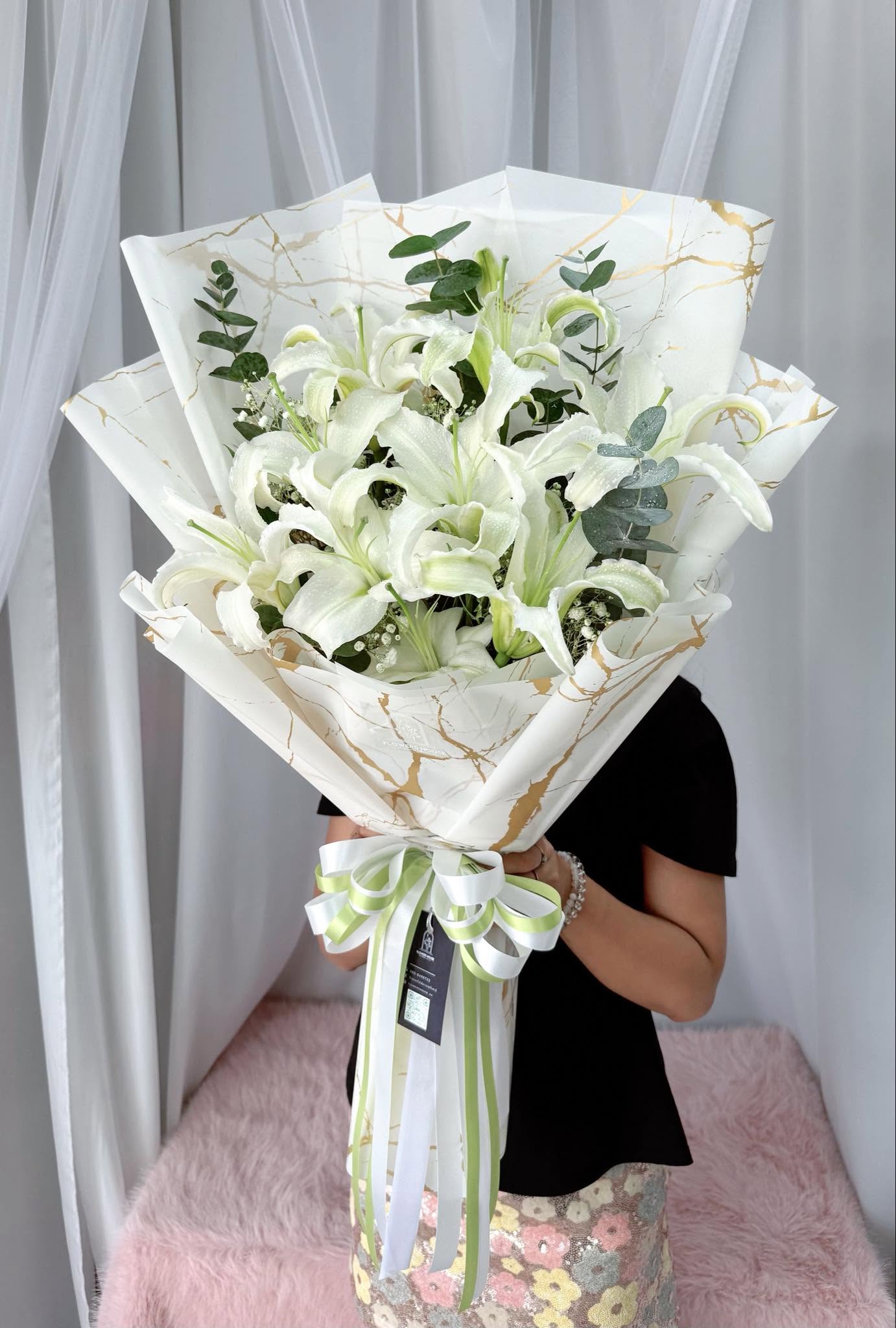 White lilies with eucalyptus and gypsophila in a white and gold marbled wrap, tied with white and green ribbon
