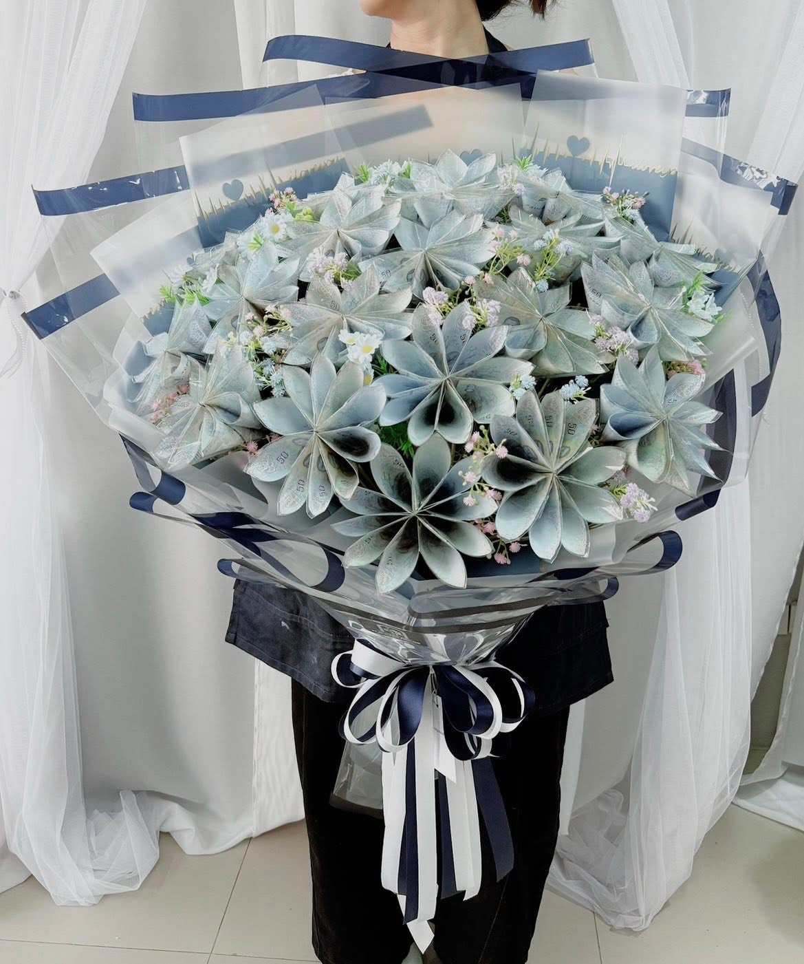 Oversized money bouquet of folded banknote flowers with gypsophila, clear wrap and navy and white ribbons